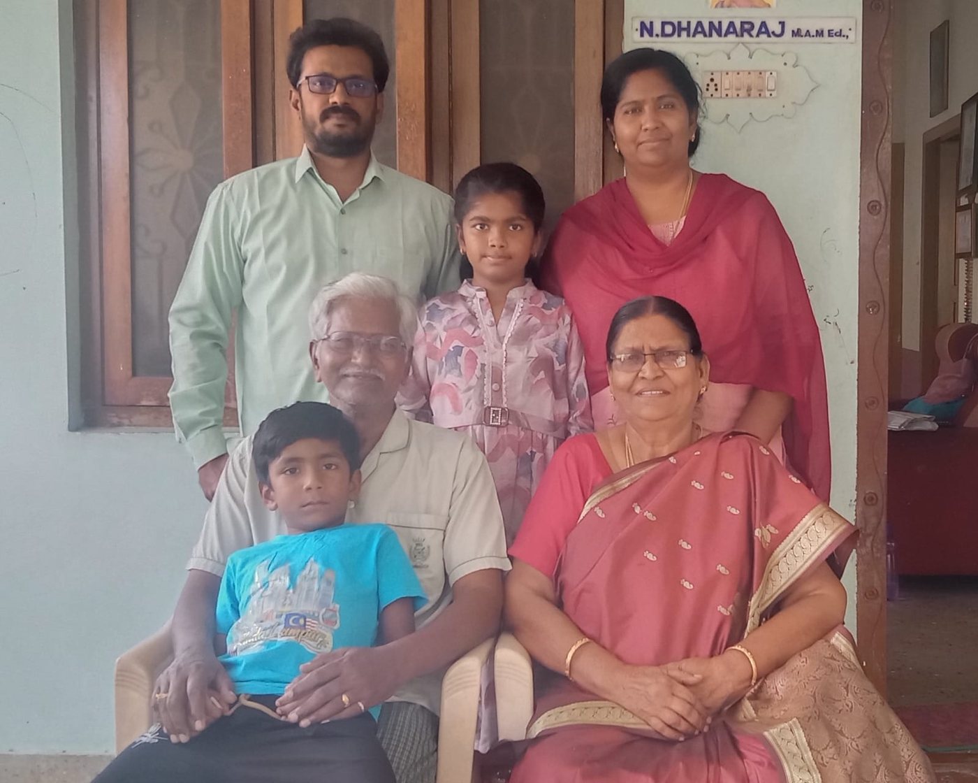 Dr. N. Dhanaraj at home in Dharapuram with his family, beside the nameboard reading N. Dhanaraj M.A., M.Ed.