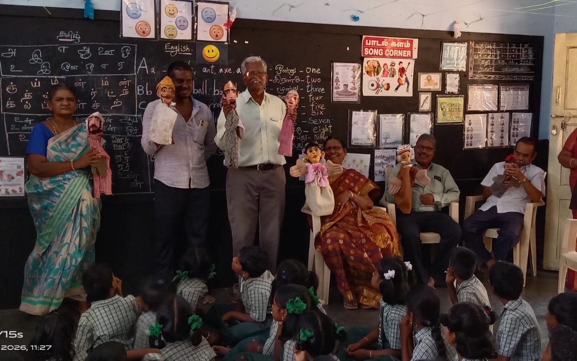 A classroom puppetry session — teachers and visitors holding glove puppets before the children